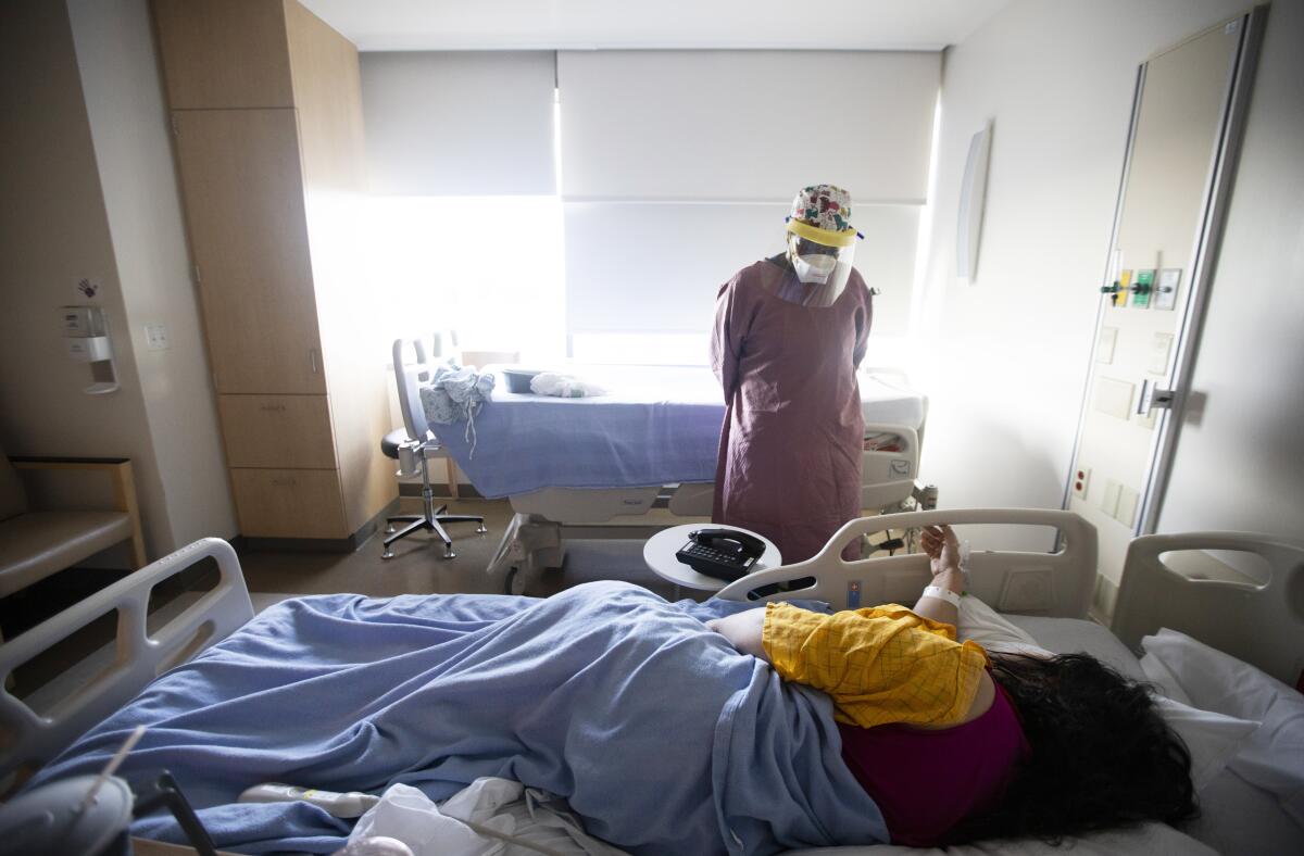 A nurse in a mask and face shield stands beside the bed of a patient