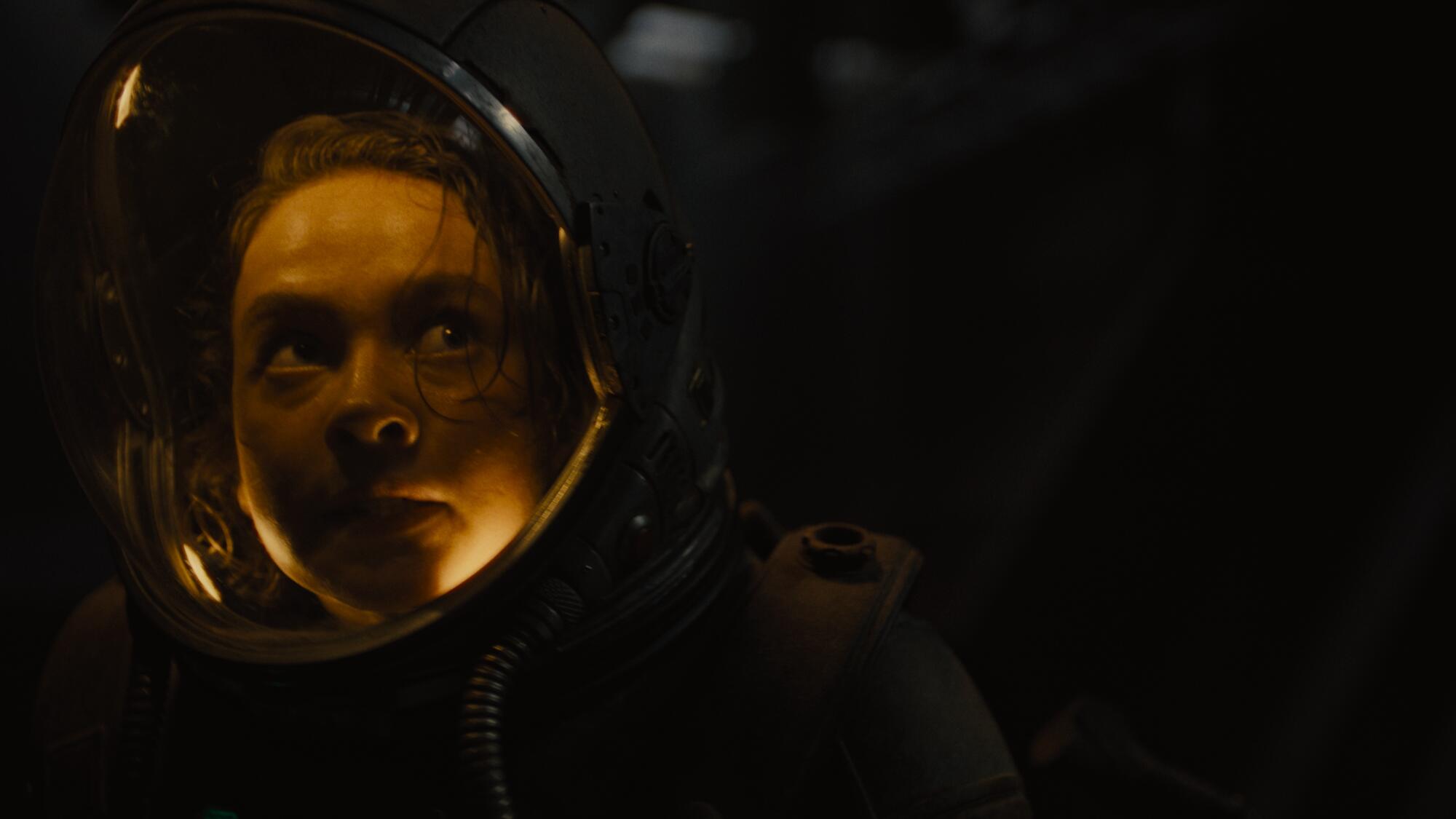 A woman in a space helmet looks over her shoulder.