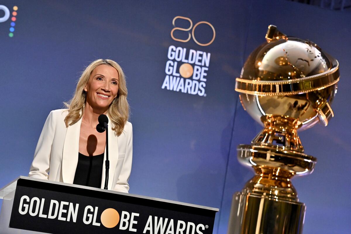 A woman in a white jacket smiles behind the podium that reads Golden Globe Awards, with a giant award to her right.