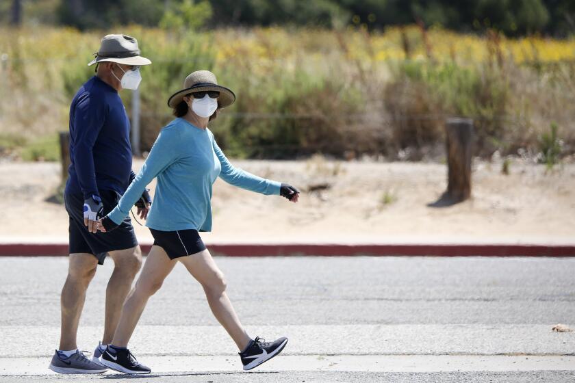 Walkers use their face coverings outddors at Fairview Park in Costa Mesa on Saturday, May 16, 2020. The park opened May 9 for activities like walking, running and cycling.