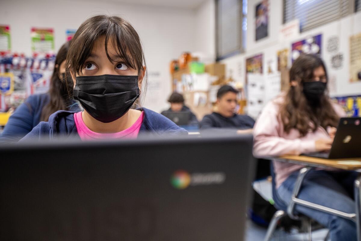 Wearing a mask, an eighth-grader  listens to her teacher 