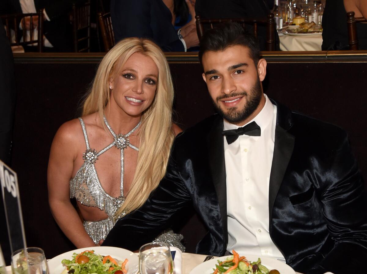 Britney Spears and Sam Ashgari in formalwear smile while sitting at a table