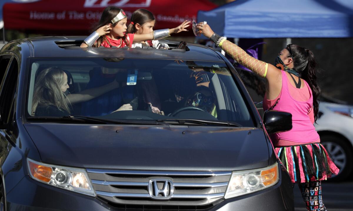 Jennifer Olivas hands treats to 6-year-old twins Loucia Ramirez, left, and Adriana Ramirez in Monterey Park.