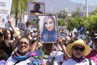 A crowd of people hold up large photos of people
