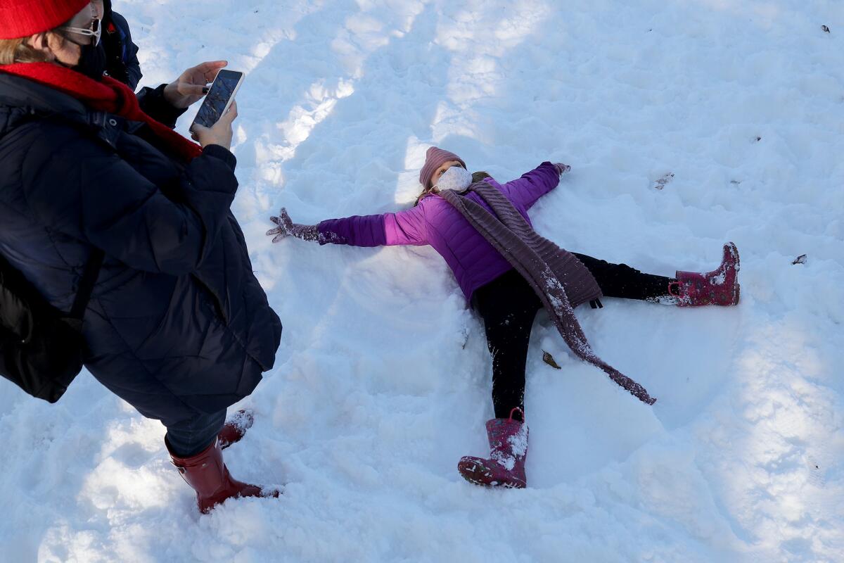 Kate Thomas, 10, forms a snow angel as her mother, Erica, left, takes a picture.