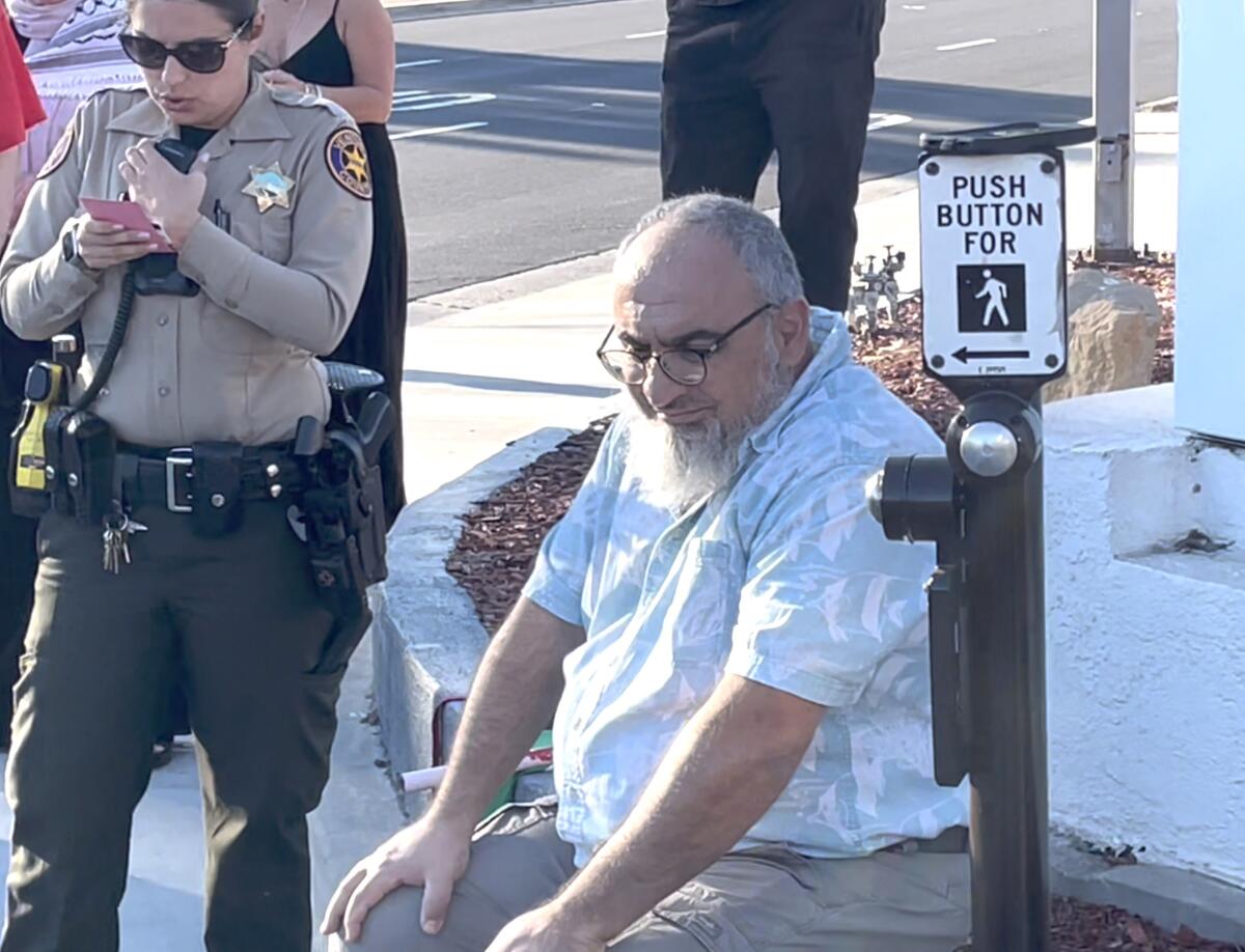 Loay Alnaji sits at a street corner, with a sheriff's deputy standing nearby