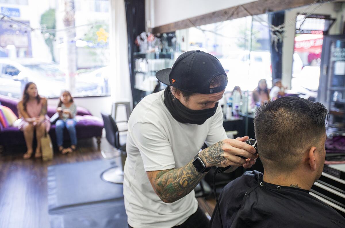 James Coelho wears a mask while giving a haircut to Ramon Ramirez from San Pedro at Makin Waves Salon in Huntington Beach on Tuesday.