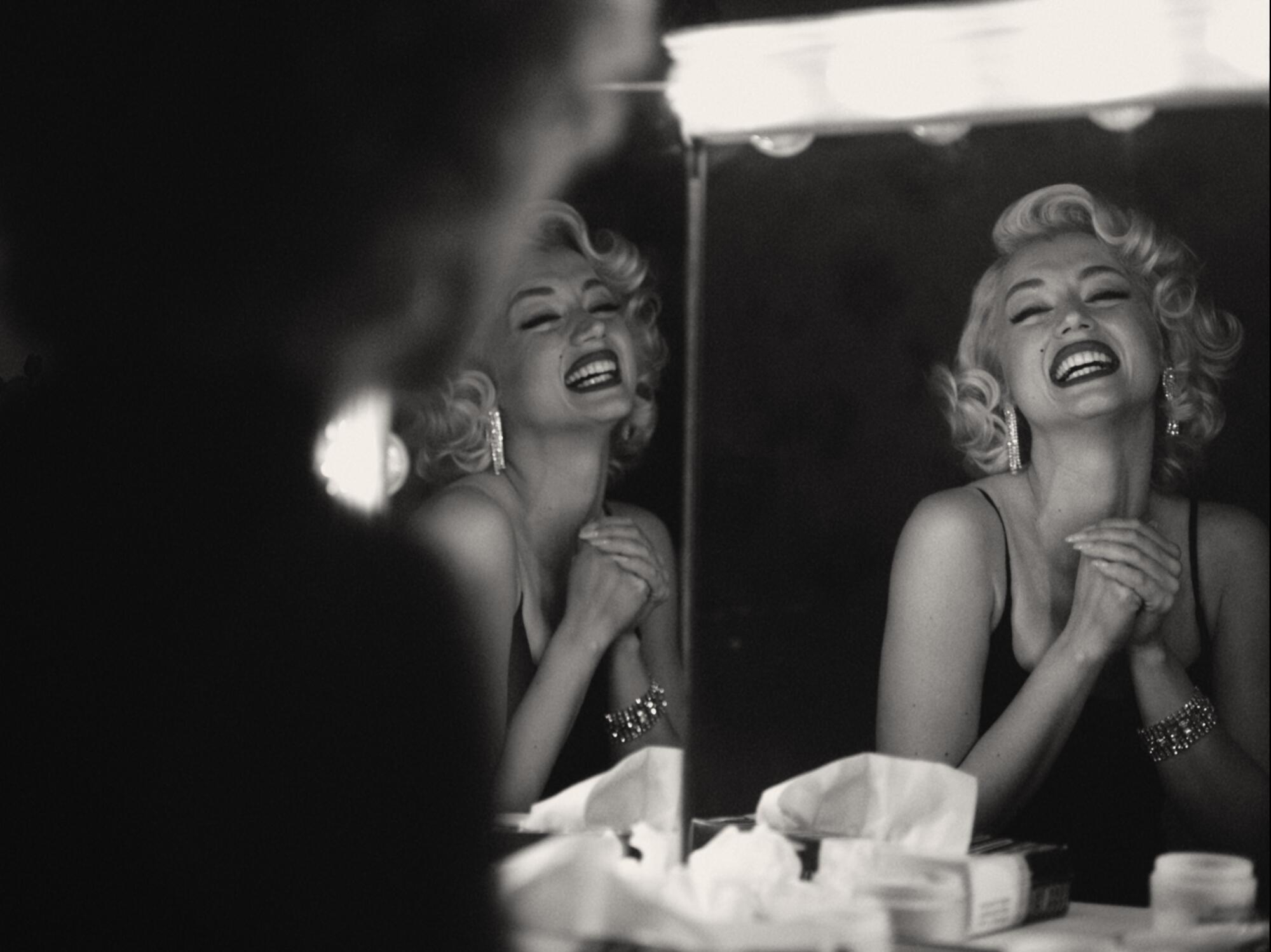 A black-and-white image of a blond woman smiling into a mirror in a scene from "Blonde."