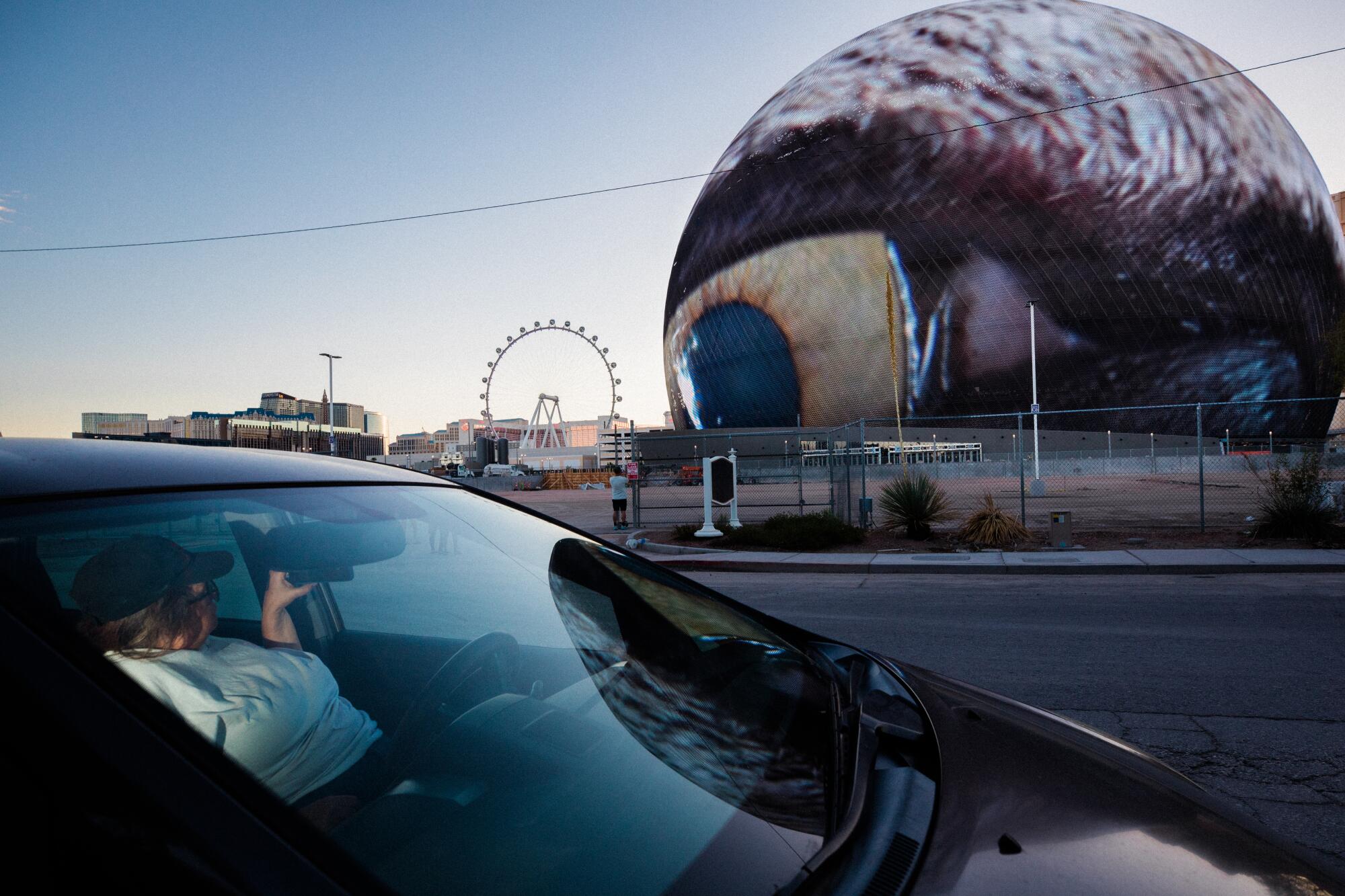 A spherical building broadcasting an eyeball that seems to peer into a passersby car.