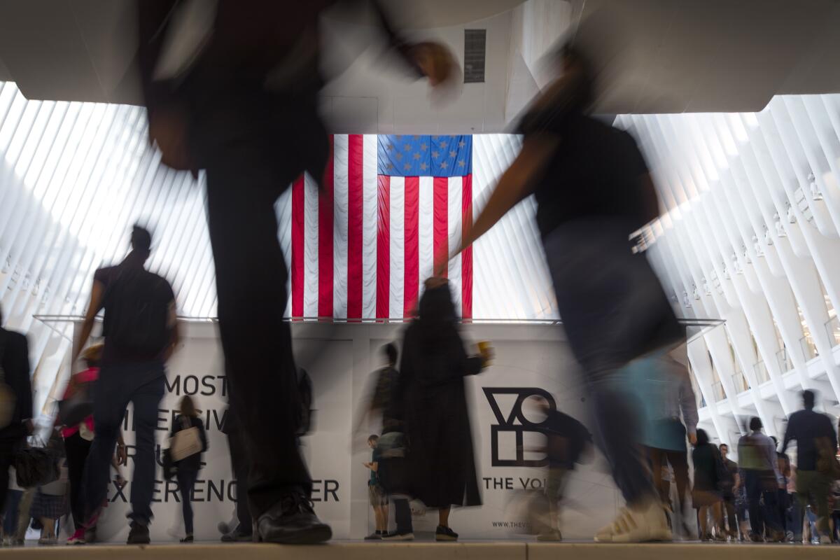 Varias personas caminan frente a la bandera de Estados Unidos dentro de Oculus,