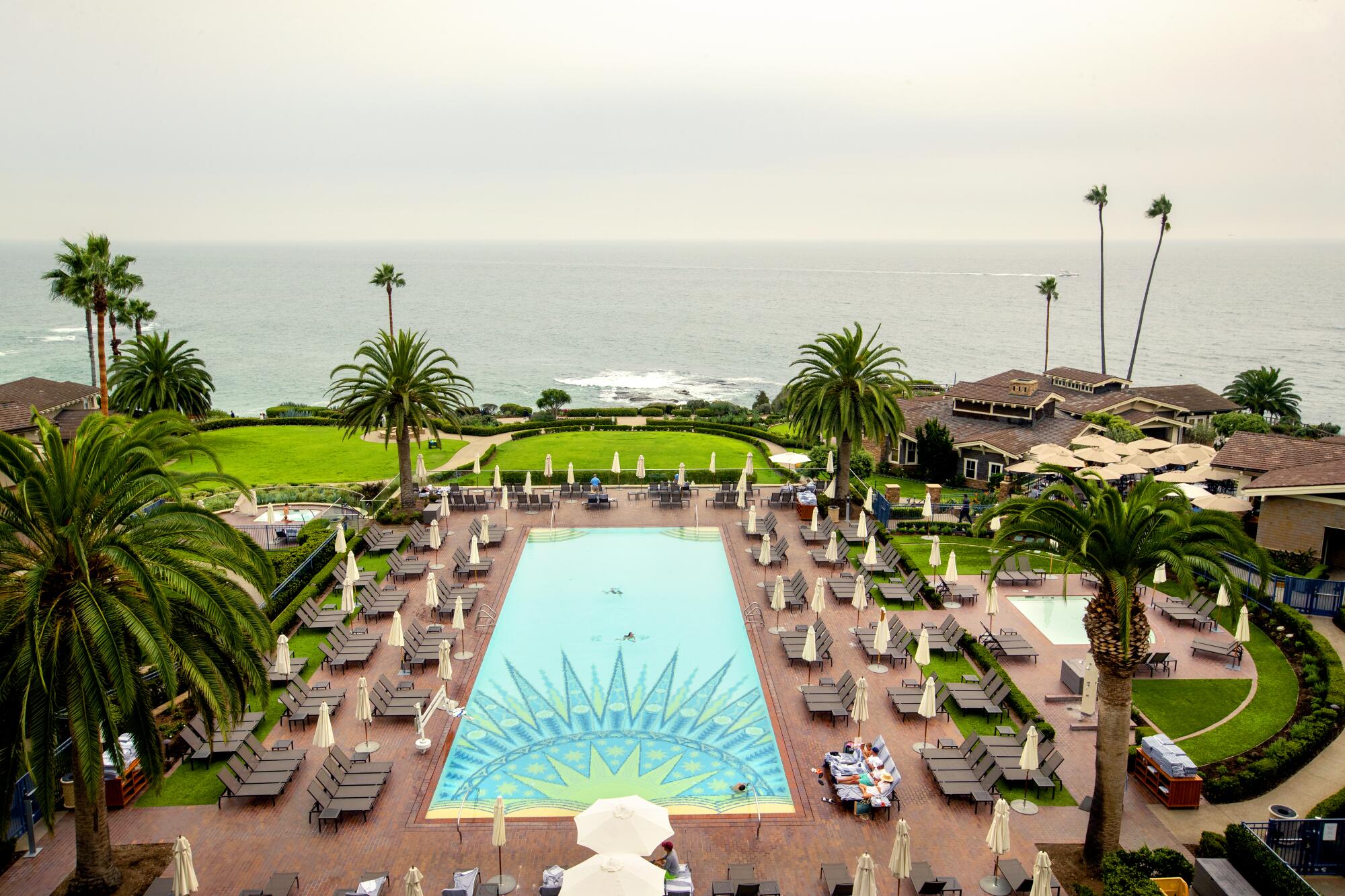 Guests swim in a pool overlooking a beach near the Pacific Ocean.