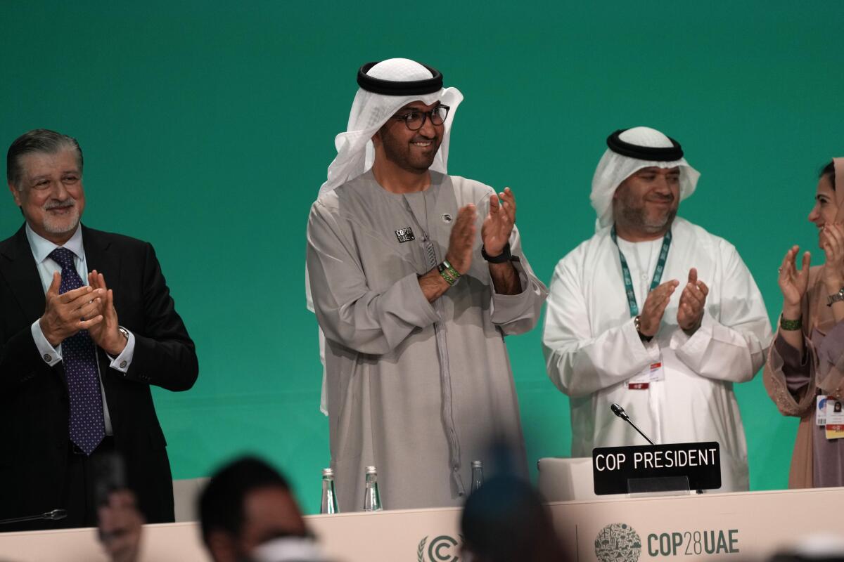 COP28 President Sultan Al Jaber claps with other people standing near him. 