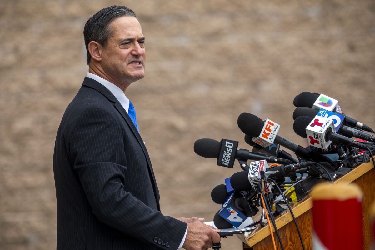 Orange County District Attorney Todd Spitzer speaks at a lectern with news microphones