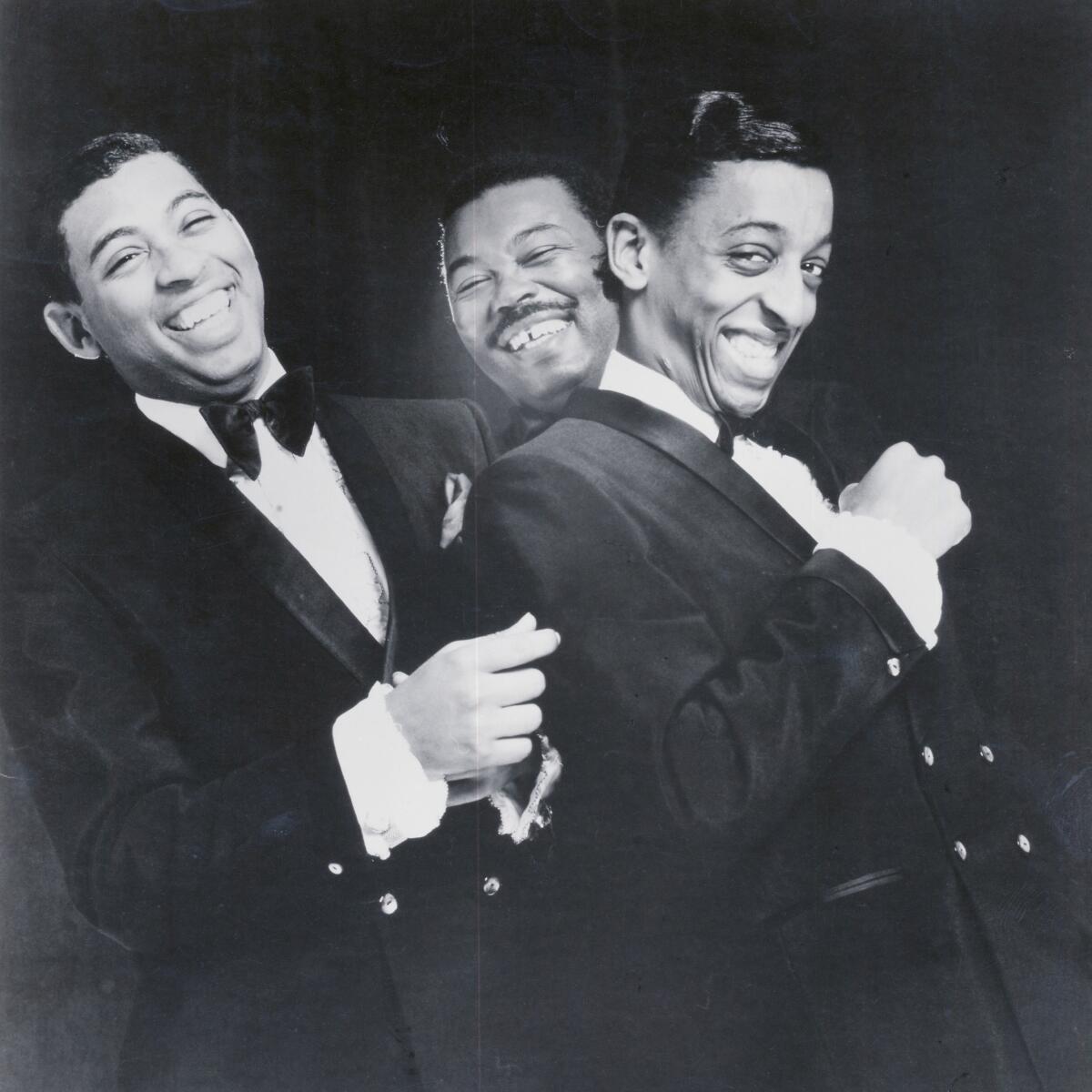 Three Black men in formalwear pose together in a black-and-white promotional image from 1963