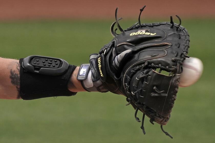 Seattle Mariners catcher Tom Murphy wears a wrist-worn device used to call pitches as he catches a ball during the sixth inning of a spring training baseball game against the Kansas City Royals, Tuesday, March 29, 2022, in Peoria, Ariz. The MLB is experimenting with the PitchCom system where the catcher enters information on a wrist band with nine buttons which is transmitted to the pitcher to call a pitch. (AP Photo/Charlie Riedel)