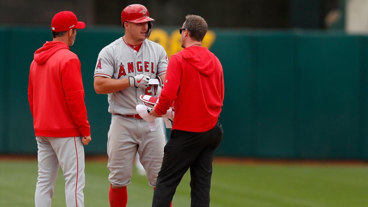 Mike Trout, center, talks with an Angels trainer and manager Brad Ausmus, left, after the outfielder felt a cramp in his leg against the Oakland Athletics.
