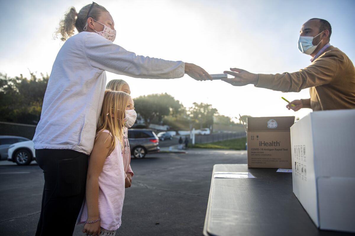 A woman stands in a parking lot with two young girls as a man behind a table hands her a small box.