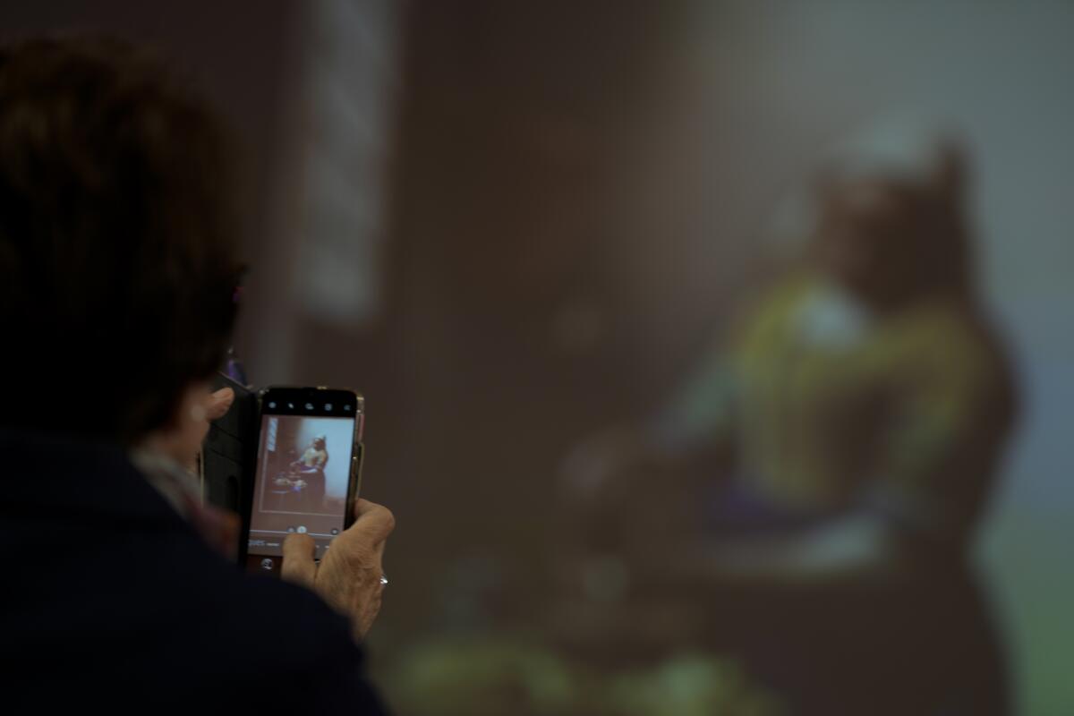 A woman takes images of a projection of Vermeer's The Milkmaid during a press conference at the Rijksmuseum in Amsterdam, Netherlands, Thursday, Sept. 8, 2022. In an unprecedented blockbuster exhibit, from Feb. 10, to June 4, 2023, the Rijksmuseum will unite two iconic paintings from Dutch artist Johannes Vermeer, The Girl with a Pearl Earring and The Milkmaid, together with 27 of the 35 known paintings of the 17th century artist who had the uncanny genius of letting a soothing inner light exude from his canvas. (AP Photo/Peter Dejong)