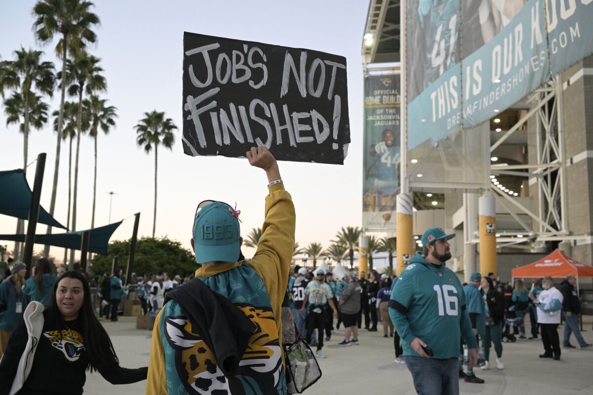 A Jacksonville Jaguars fan holds a homemade sign that reads "Job's Not Finished" outside TIAA Bank Field