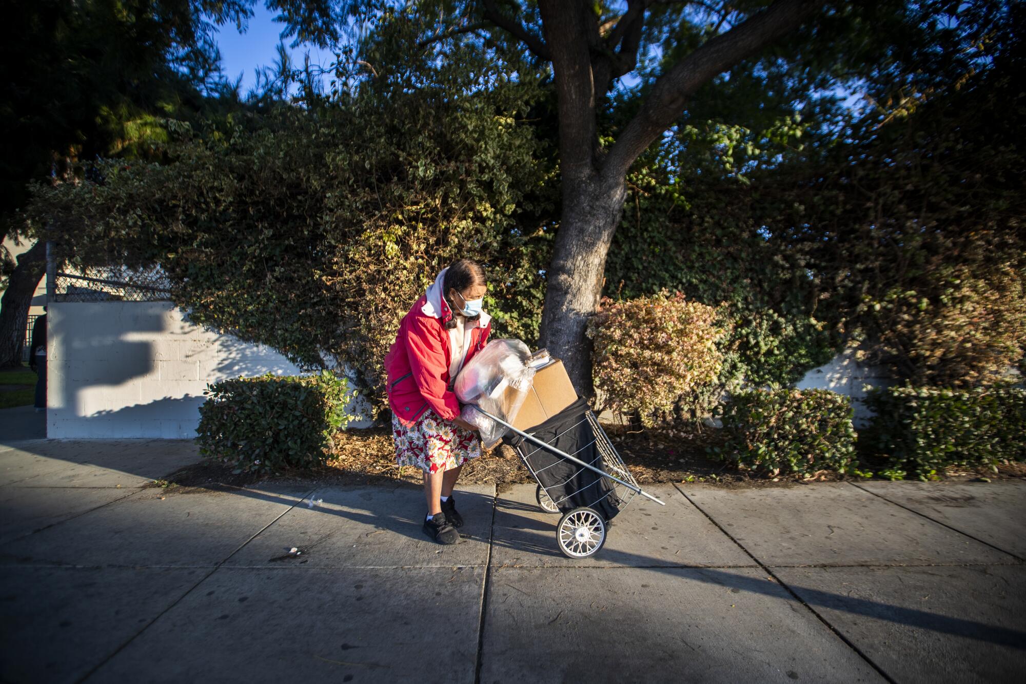 A woman bends over to get a handle on her push cart loaded with meals