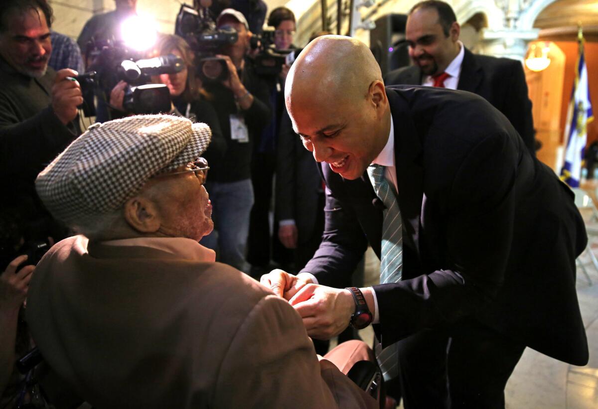 Newark Mayor Cory Booker pins New Jersey's Meritorious Service Medal onto the chest of 90-year-old World War II veteran Willie Wilkins at Newark City Hall. Booker, who is running for U.S. Senate, honored the veteran on the anniversary of Victory in Europe Day.