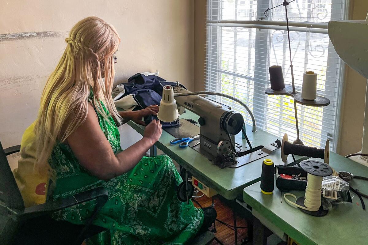 A woman sits at a sewing machine facing a window