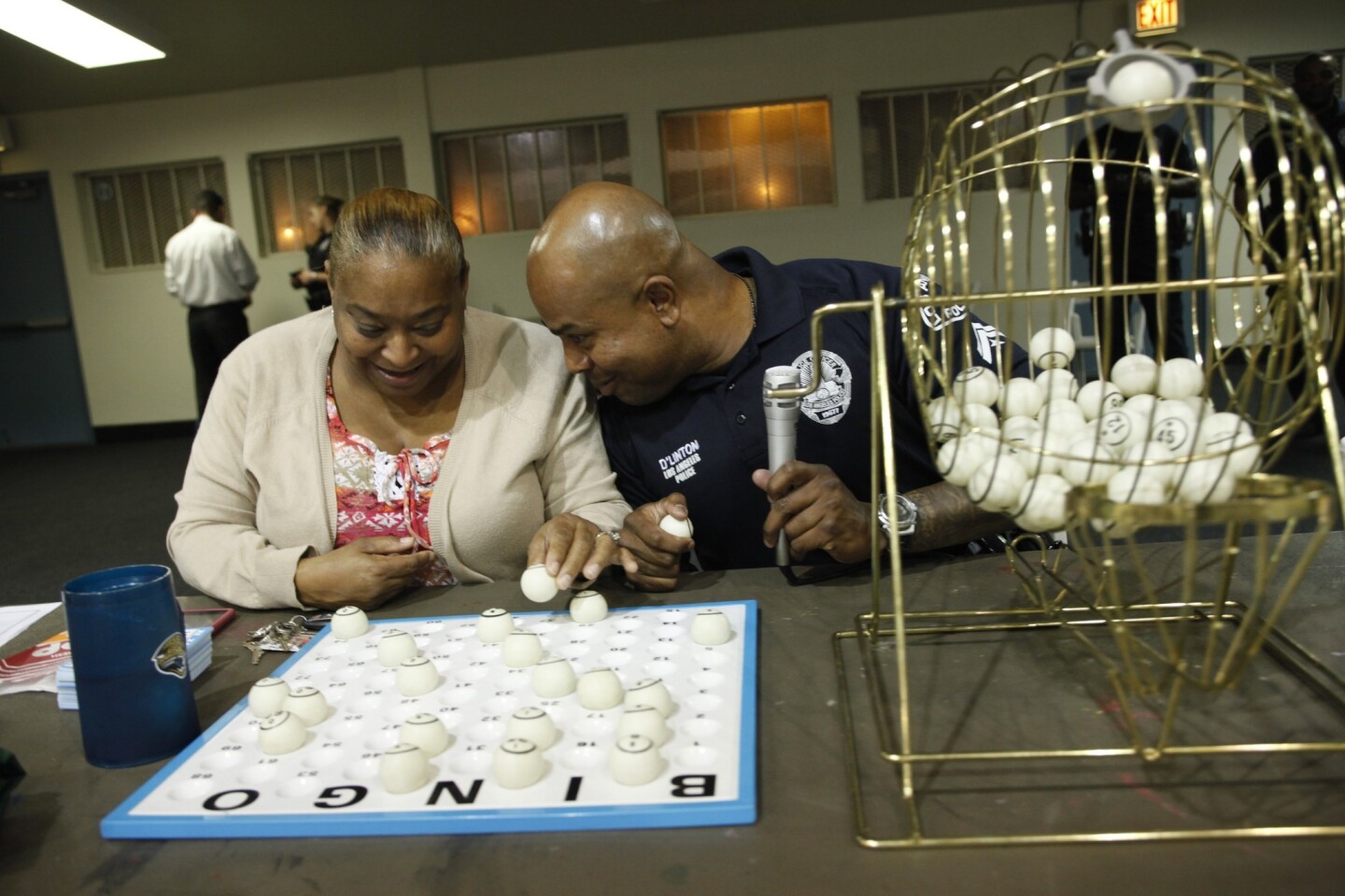 Kathy Wooten helps call bingo numbers with Officer Keith Linton at a bingo night in the Jordan Downs gym hosted by LAPD officers.