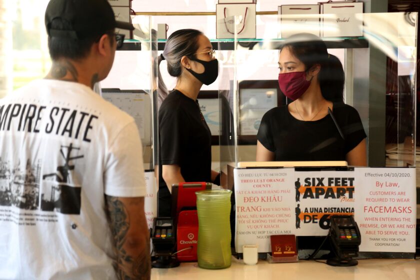 FOUNTAIN VALLEY, CA - APRIL 20, 2020 - Kayla Le, center, and Nguyen Nguyen, right, both wearing protective masks and gloves, take orders at Brodard Restaurant in Fountain Valley on April 20, 2020. Brodard's is one of Orange County's most famous Vietnamese Restaurants and is still doing take-out orders since the coronavirus shutdown many businesses. All employees wear safety masks and gloves and customers are required to wear a mask, but some do not comply. (Genaro Molina / Los Angeles Times)