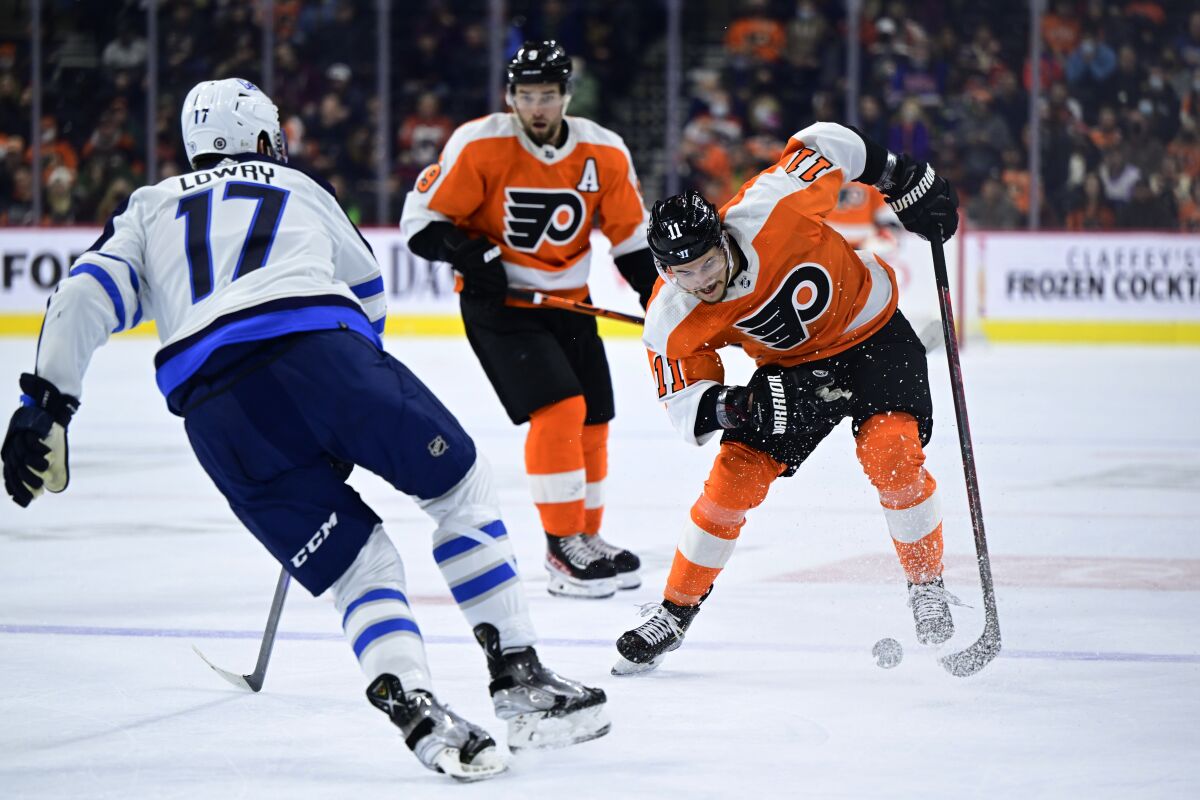 Philadelphia Flyers' Travis Konecny, right, skates up ice with the puck against the defense of Winnipeg Jets' Adam Lowry (17) during the second period of an NHL hockey game Tuesday, Feb. 1, 2022, in Philadelphia. (AP Photo/Derik Hamilton)