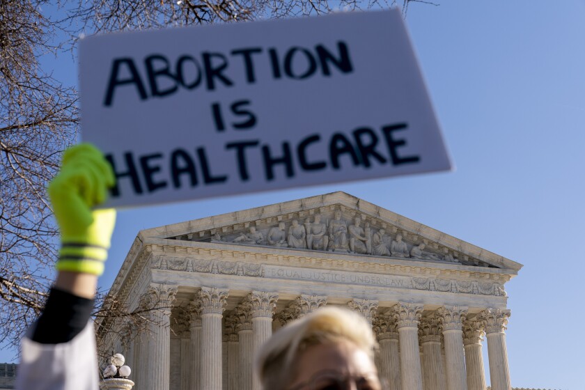 A woman in an doctors uniform holds a poster that reads "Abortion is Healthcare" as abortion rights advocates and anti-abortion protesters demonstrate in front of the U.S. Supreme Court, Wednesday, Dec. 1, 2021, in Washington, as the court hears arguments in a case from Mississippi, where a 2018 law would ban abortions after 15 weeks of pregnancy, well before viability. (AP Photo/Andrew Harnik)