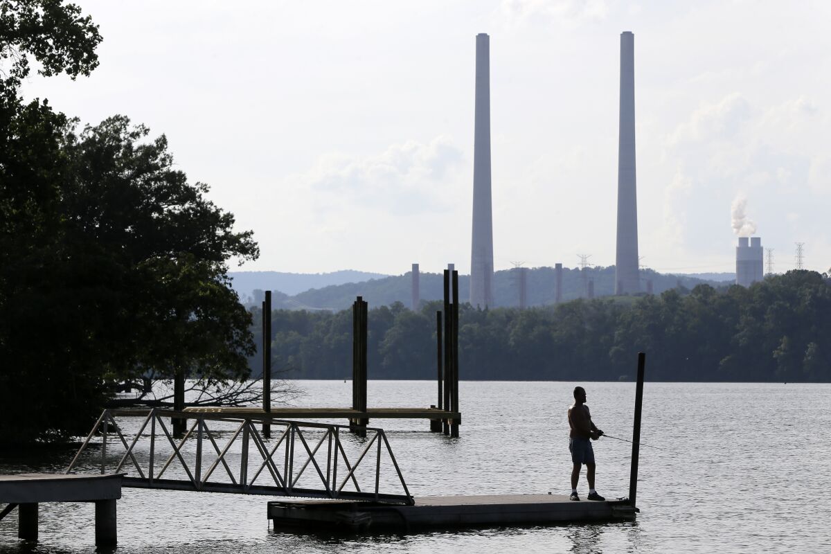 FILE - In this Aug. 7, 2019, file photo, a man fishes at William B. Ladd Park near the Kingston Fossil Plant in Kingston, Tenn. The largest public power company in the U.S. is launching a program to develop and fund new small modular nuclear reactors as part of its strategy to dramatically reduce greenhouse gas emissions. The board for the Tennessee Valley Authority on Thursday, Feb. 10, 2022 authorized the program to assess moving forward with new nuclear technology, with up to $200 million to be spent for the first phase. (AP Photo/Mark Humphrey, File)