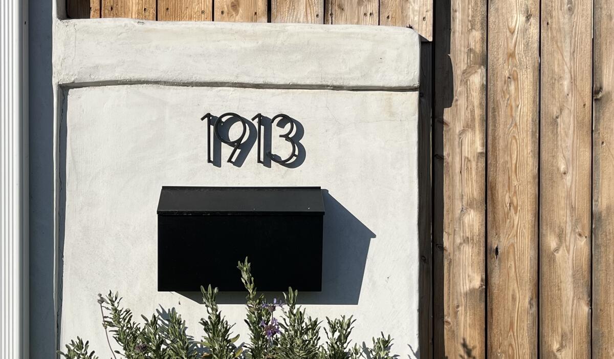 A house number, 1913, in a stylish dark font above a black mailbox mounted against a cream background over wood siding