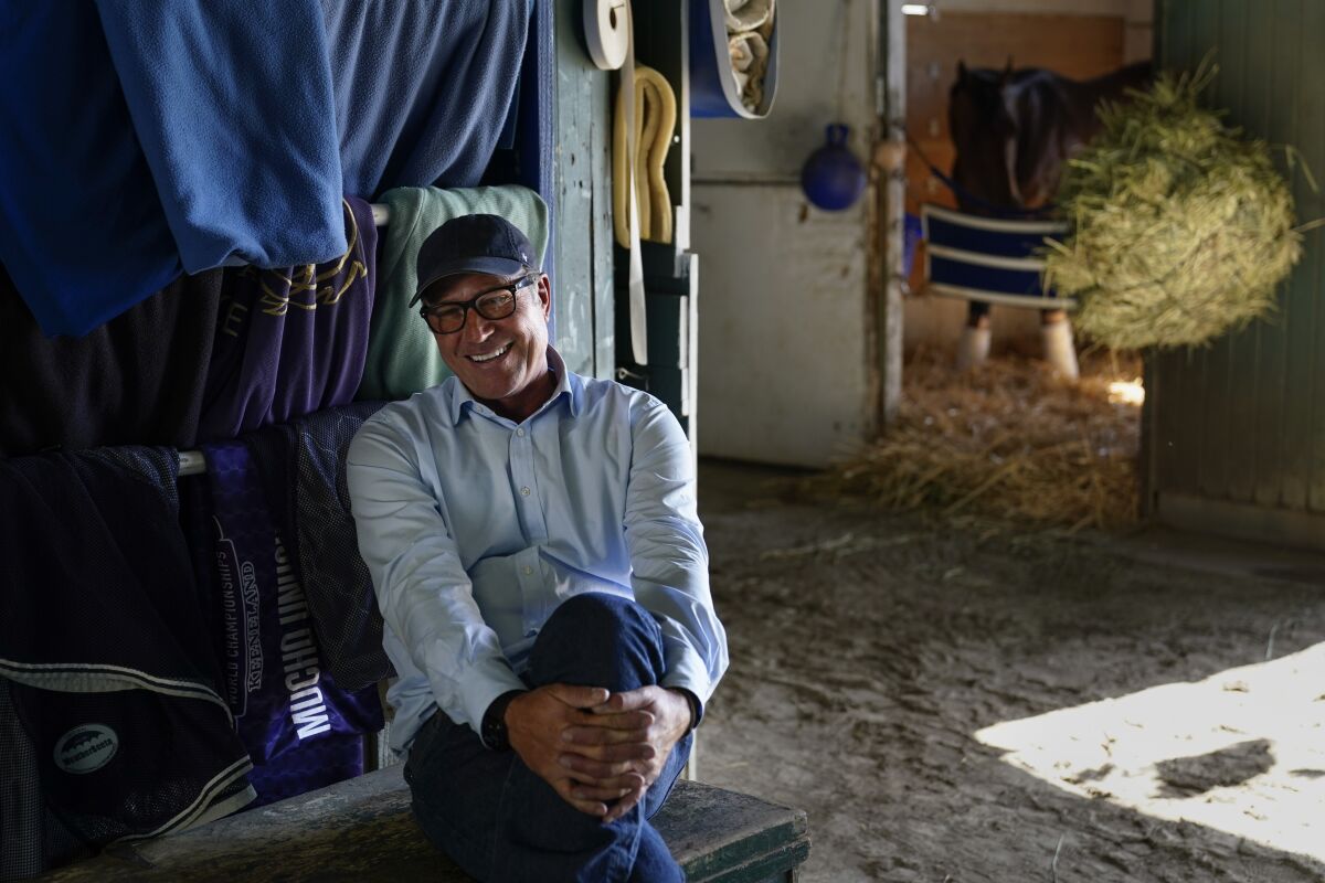 Tim Yakteen smiles in his horse barn at Santa Anita Park on Monday, April 25, 2022, in Arcadia, Calif. He will saddle two horses - Messier and Taiba, both formerly trained by Bob Baffert - for the Kentucky Derby. Baffert is serving a 90-day suspension from horse racing. (AP Photo/Ashley Landis)