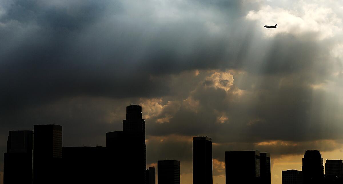 A plane flies into a shaft of sunlight as dark clouds drift inland and over downtown Los Angeles on Friday, Dec. 6, 2013.