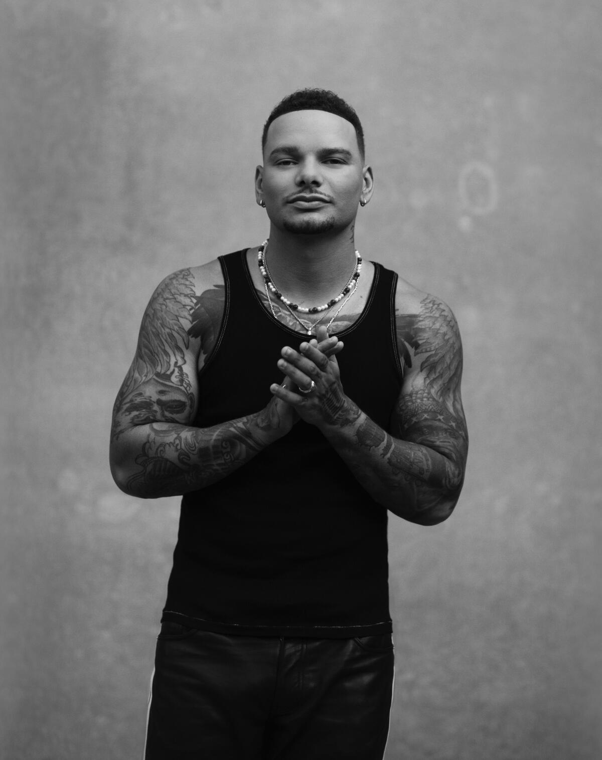 A man in a black t-shirt with many tattoos stands for a portrait