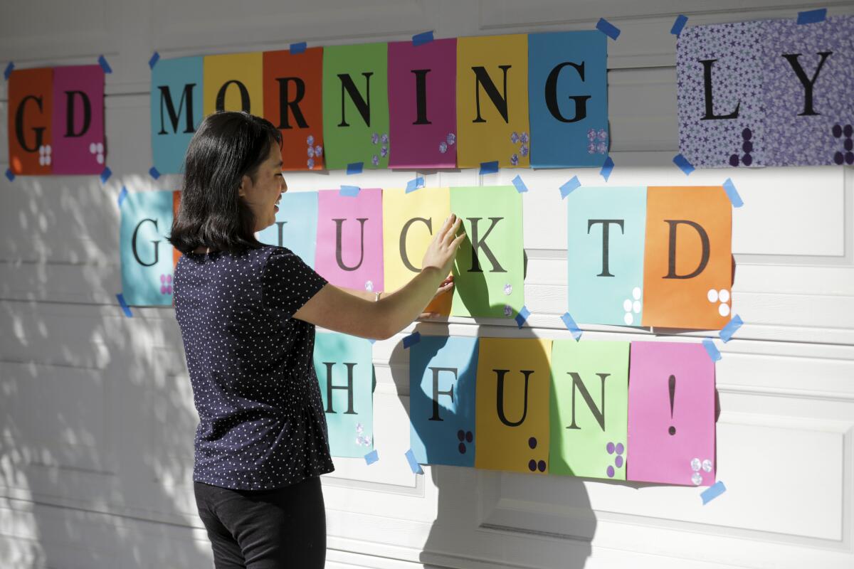 A teenager touches a colorful paper sign with Braille sticker dots on a garage door