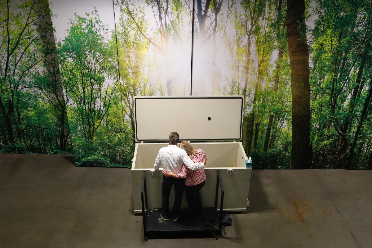 Two people stand together looking into a human composting container.