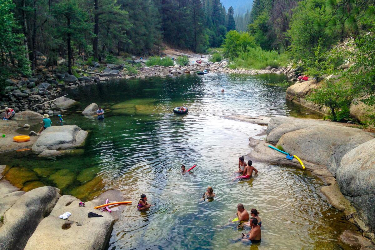 People lounge and swim in a pool of water surrounded by boulders and evergreen trees.