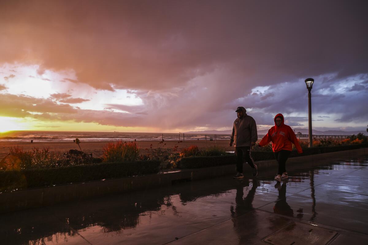 Two people walk at sunset near the beach under dark clouds