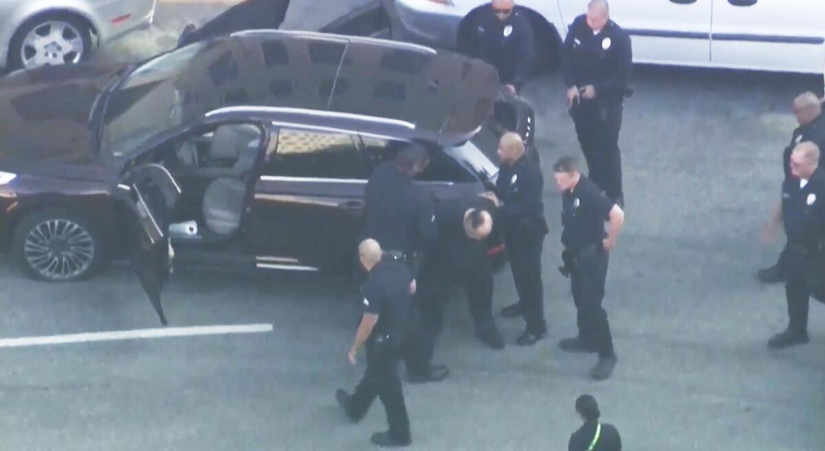 A 71-yeA man is surrounded by police officers near a parked car.