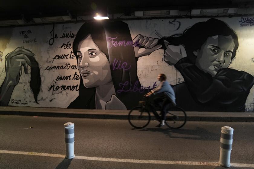 FILE - A woman rides bicycle front of a mural signed by Clacks-one and Heartcraft_Street art, depicting women cutting their hair to show support for Iranian protesters standing up to their leadership over the death of a young woman in police custody, in a tunnel in Paris, France, Wednesday, Oct. 5, 2022. The mother of a 16-year-old Iranian girl has disputed official claims, Friday, Oct. 7, that her daughter fell to her death from a high building, saying the teen was killed by blows to the head as part of the crackdown on anti-hijab protests roiling the country. Nika Shakarami has become the latest icon of the protests, seen as the gravest threat to Iran’s ruling elites in years. (AP Photo/Francois Mori)