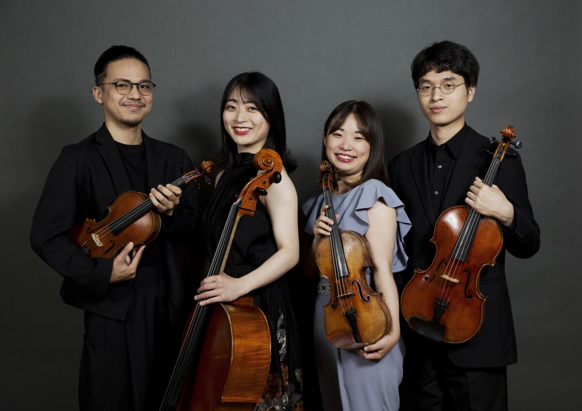 Four people posing with string instruments in front of a gray backdrop. 