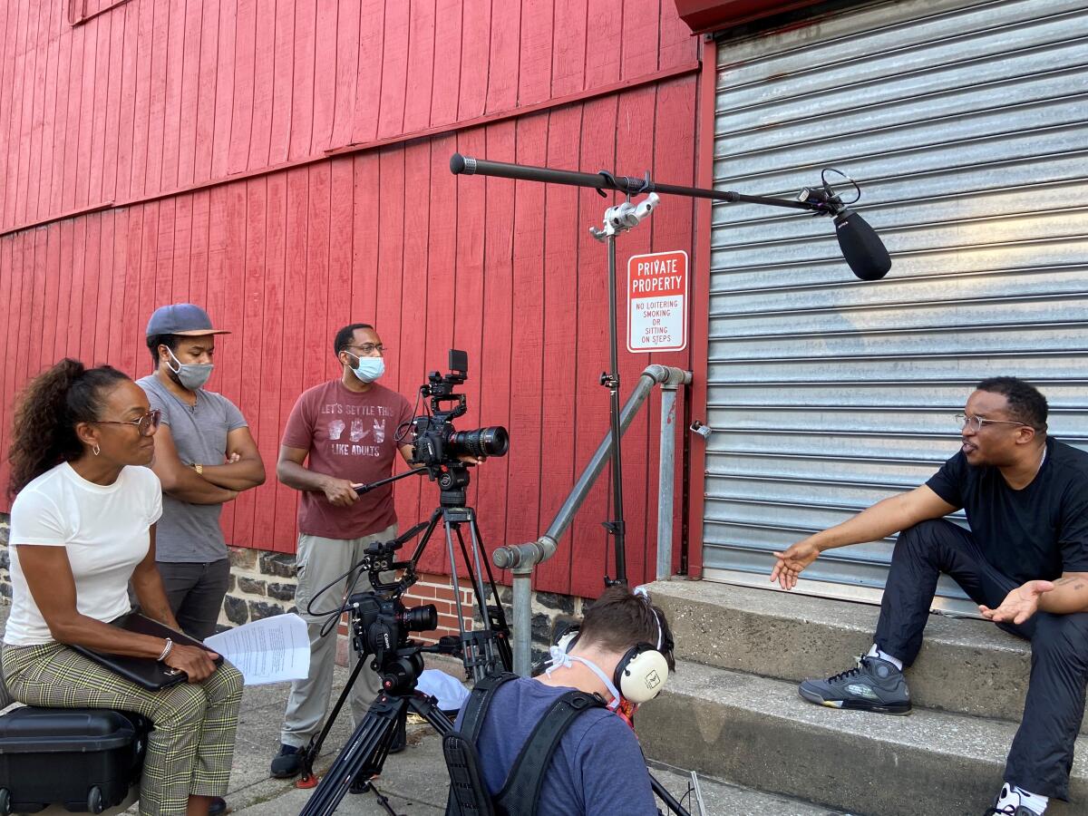 A woman interviews a man for a documentary, surrounded by the film crew