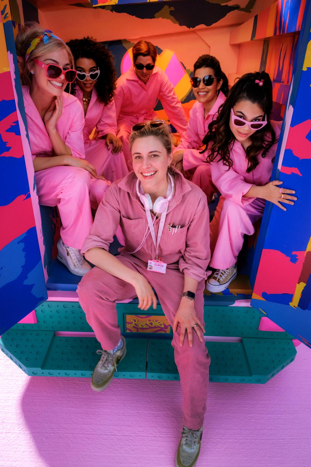 Greta Gerwig and the cast of "Barbie," all in pink uniforms, pose in the back of a pink truck from the movie