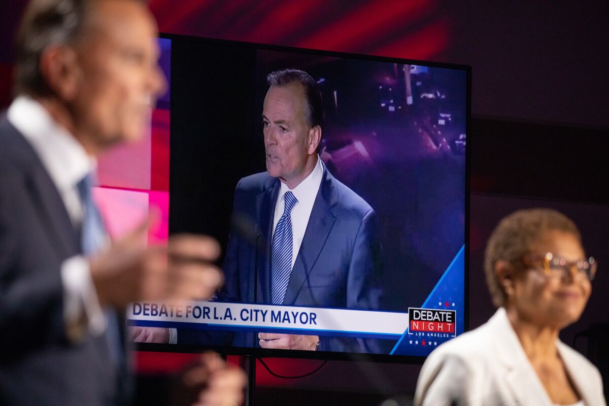 Rick Caruso appears on a television screen with Representative Karen Bass during his mayoral debate.