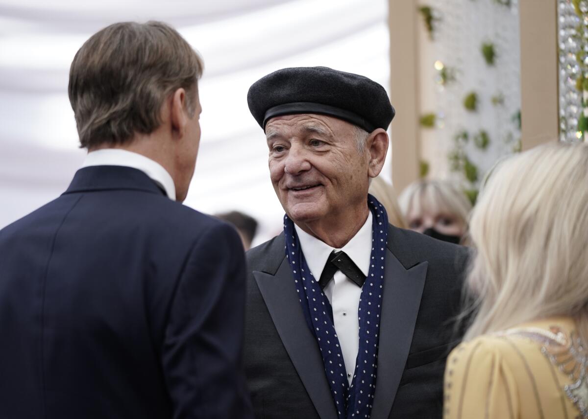A man in a suit and black beret speaking to another man in a suit