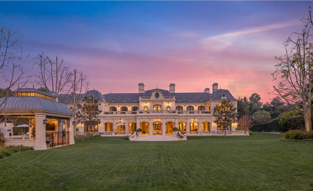 The backyard with a view of the mansion and the lawn set against a pink and blue sky.