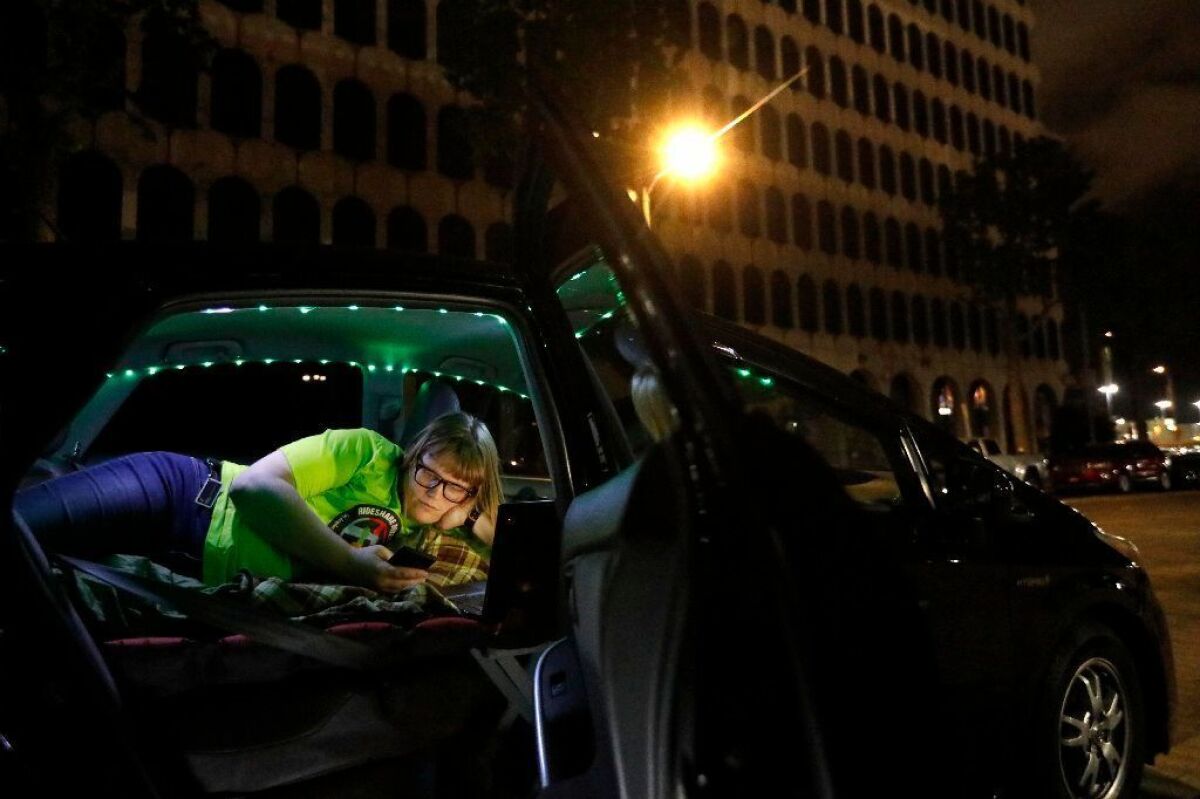 Jos Cashone, 28, looks at her phone in May before bedding down for the night in her car, which she also uses for her job as a Lyft driver.