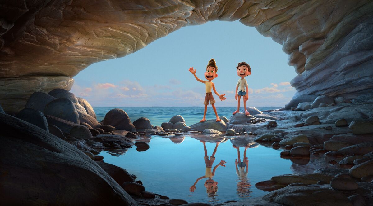 Two animated boys stand with their backs to the sea facing a cave in Pixar's "Luca."