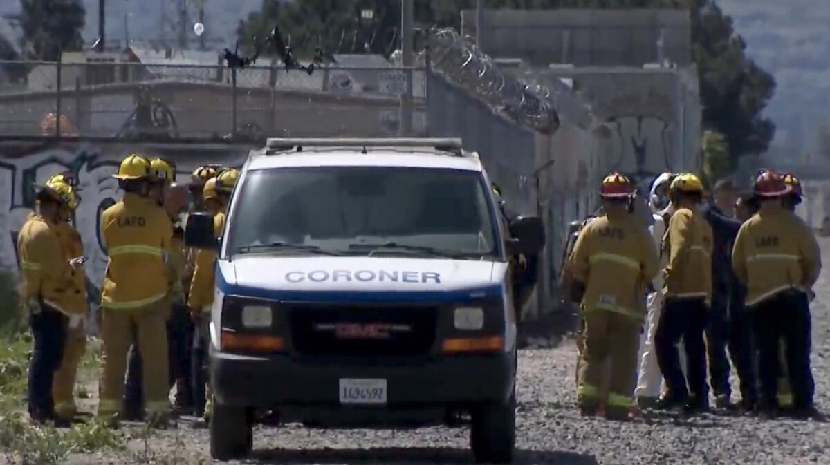 Firefighters stand around a coroner's van.